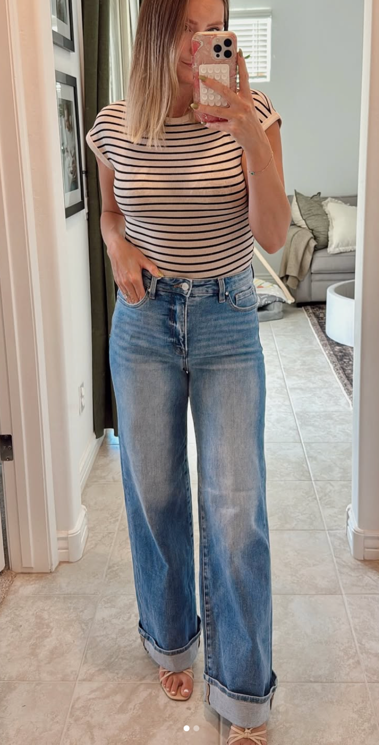 Woman taking a mirror selfie wearing a striped shirt and blue jeans in a home setting.